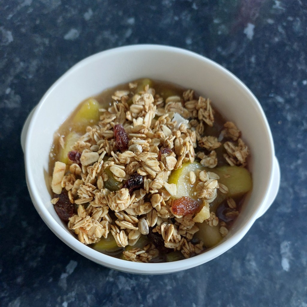 Photo of rhubarb and apple crumble filling topped with granola, in a white bowl.